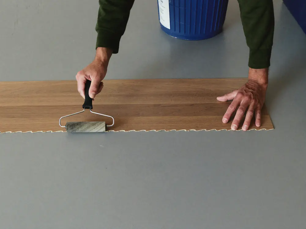 Dryback PVC plank wordt met een handrol in de lijm gedrukt