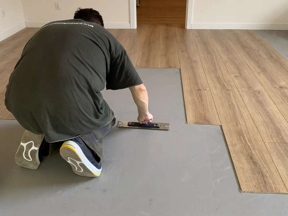 Plak-PVC plank wordt in de lijm gedrukt op een geegaliseerde dekvloer