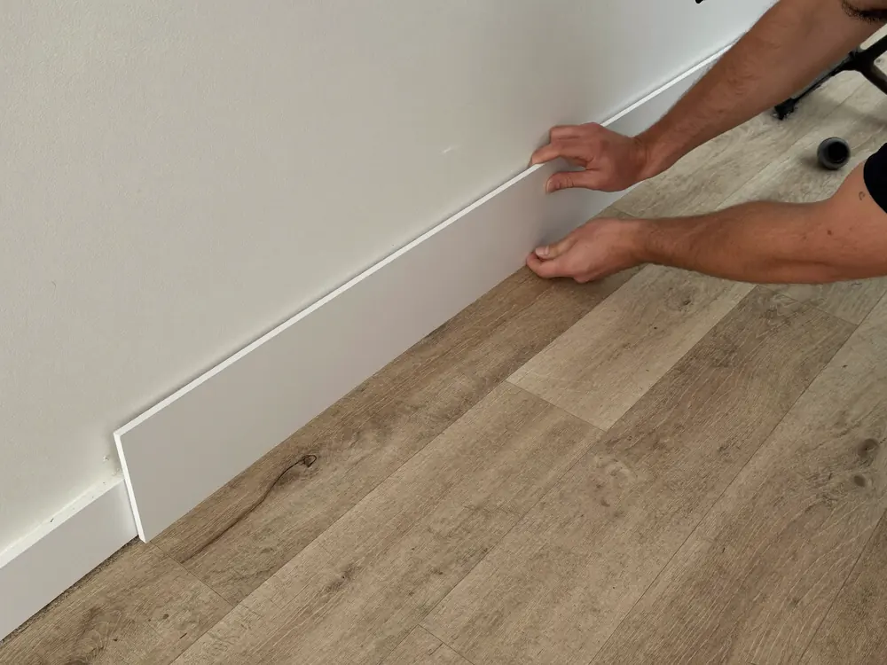 Witte plint wordt gemonteerd boven een nieuwe PVC vloer